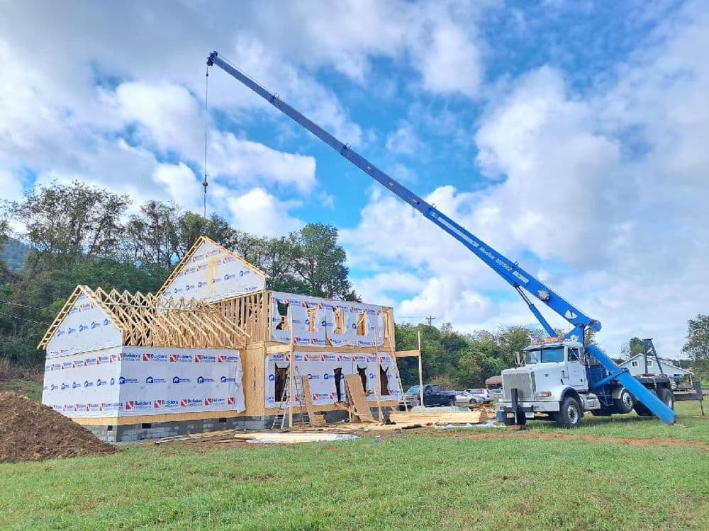 Construction site with a crane lifting materials for framing a house under blue skies.