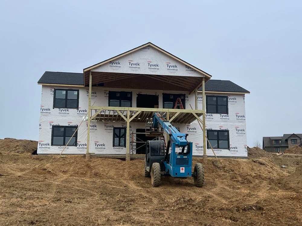 Construction site featuring a two-story house with Tyvek wrap and lift equipment.