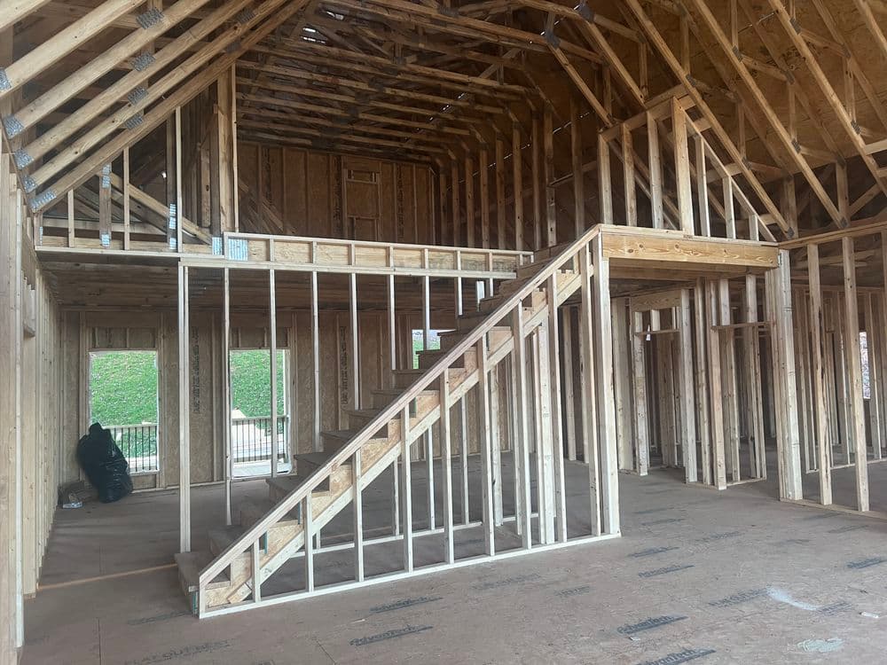 Interior of a wooden home under construction, featuring an open layout and framed staircase.