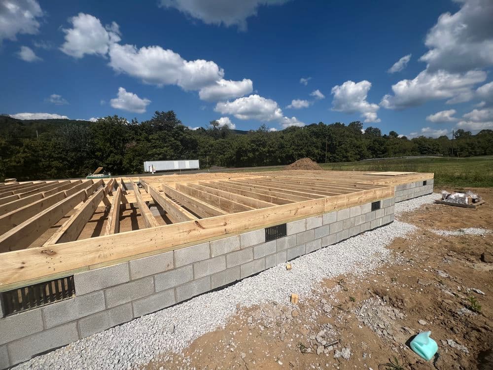 Construction site with wooden beams on concrete block foundation under a blue sky.