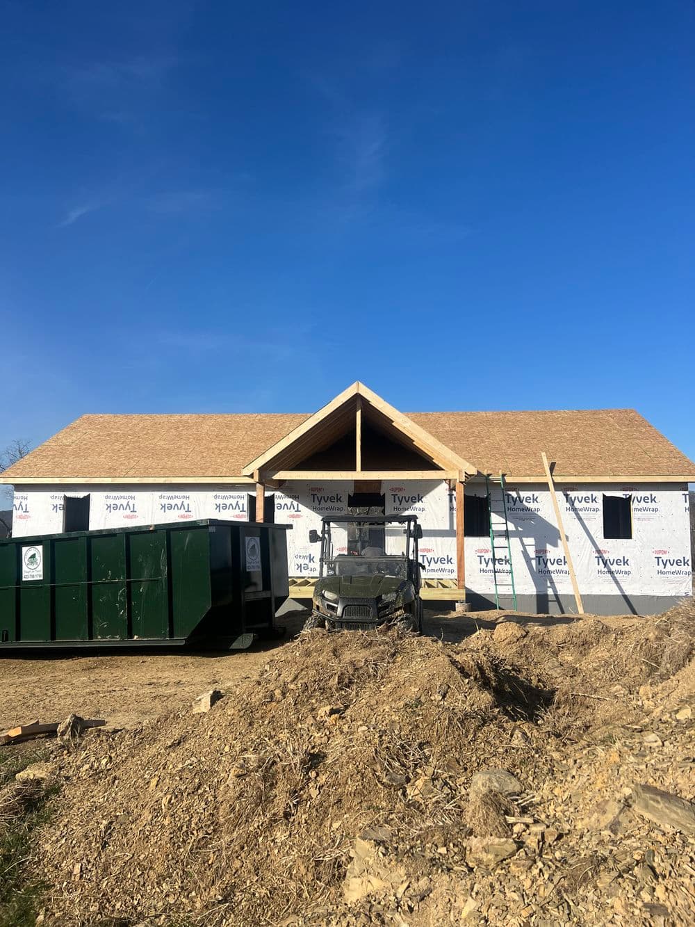 New construction home with framed entrance, Tyvek wrapping, and construction equipment on site.