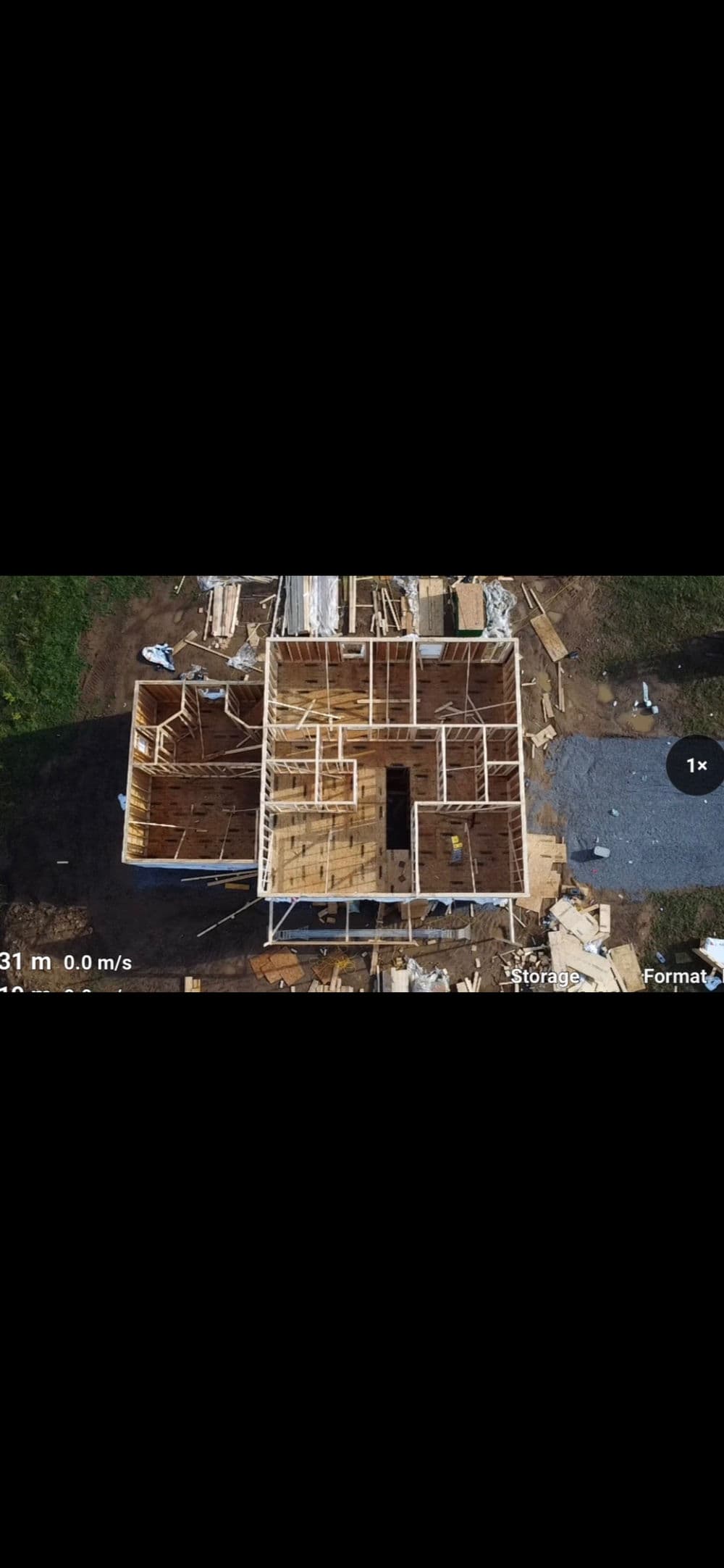 Aerial view of a house under construction with framing, lumber, and building materials visible.