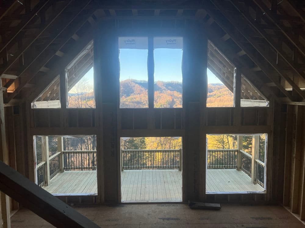 Newly framed mountain view from an unfinished attic with large windows and wooden flooring.