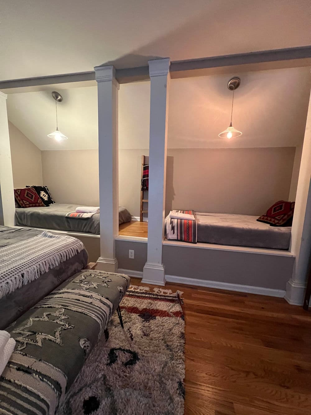 Cozy bedroom with two beds separated by columns, featuring warm lighting and decorative accents.