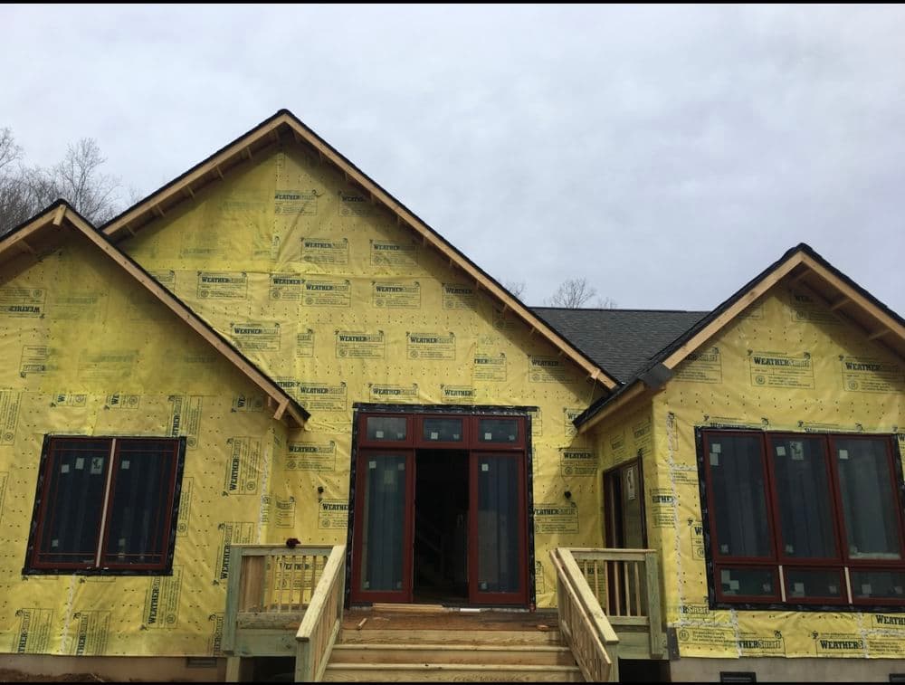 Newly constructed house with yellow insulation and wooden steps, under cloudy skies.