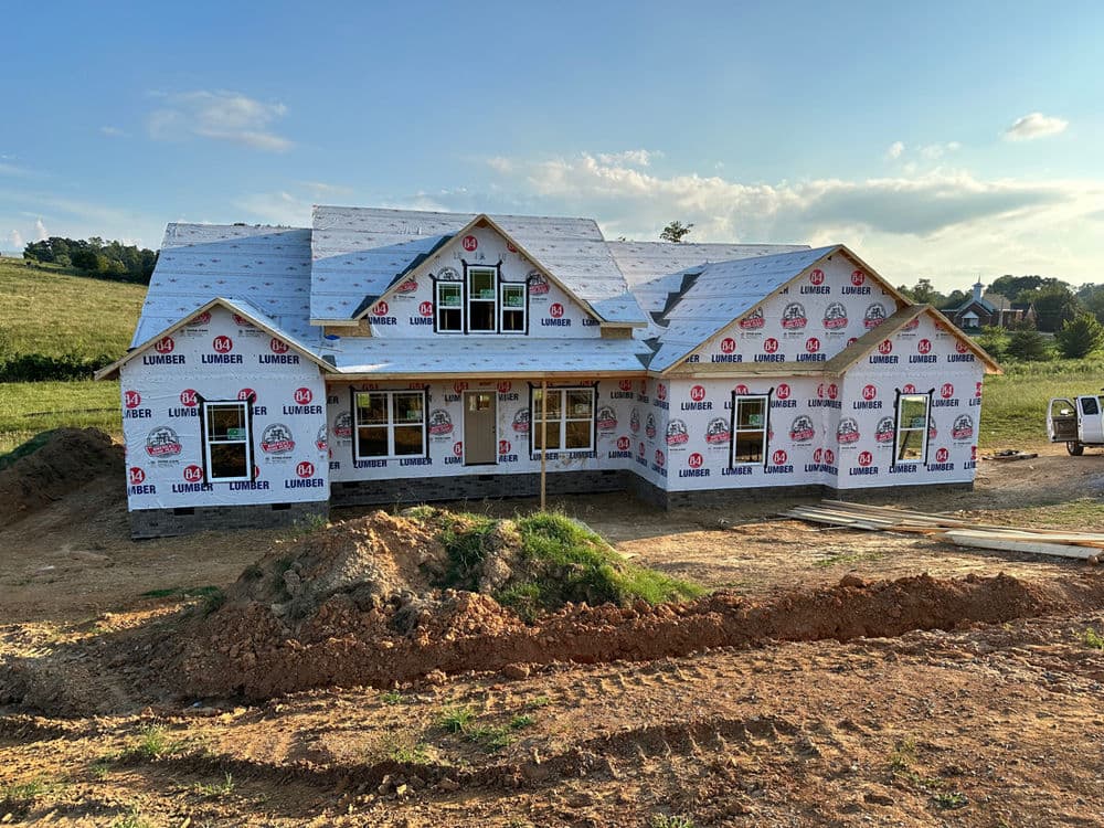 Newly constructed house with lumber wrap, surrounded by a grassy landscape, in daylight.