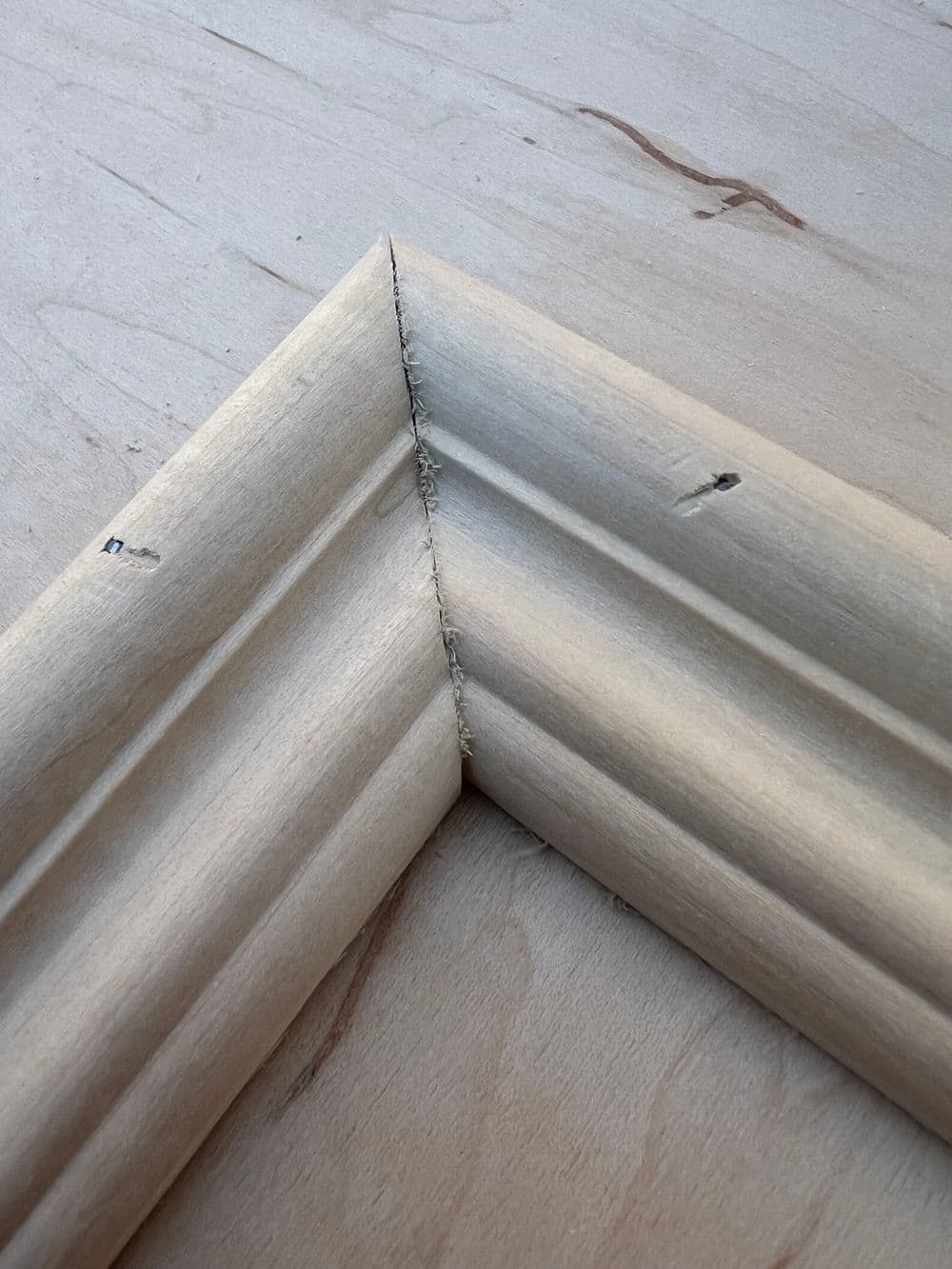 Detailed wooden picture frame corner on smooth wood surface.