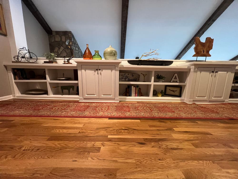 Modern wooden living room shelving with decor items and a rustic red area rug.