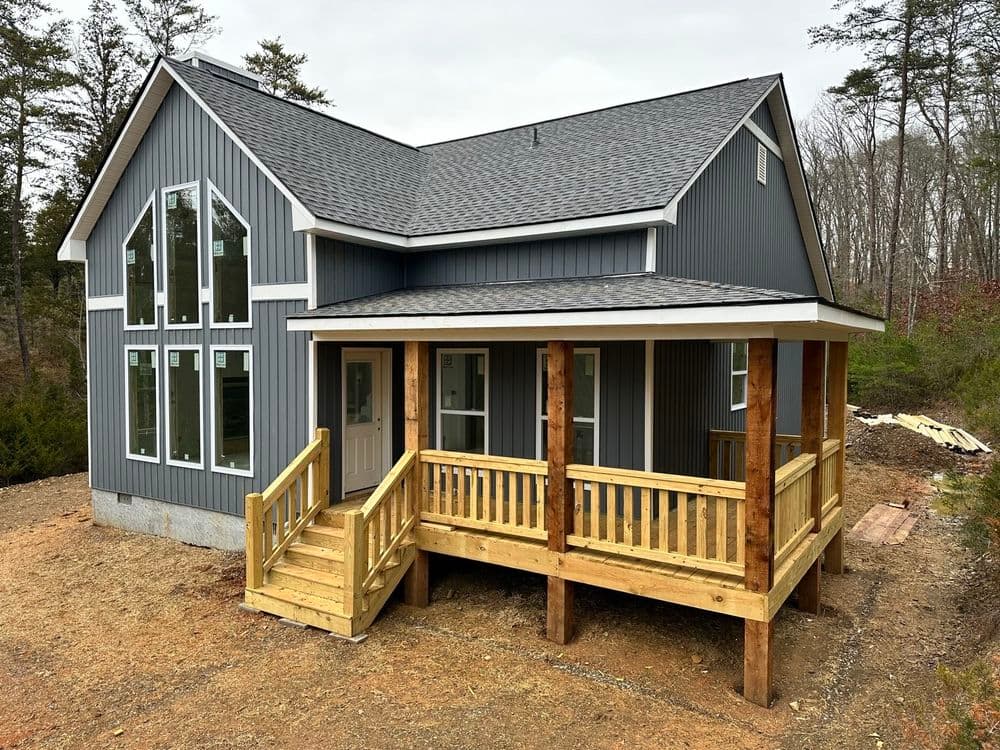 Modern gray house with wooden porch and ramp, surrounded by trees in a natural setting.