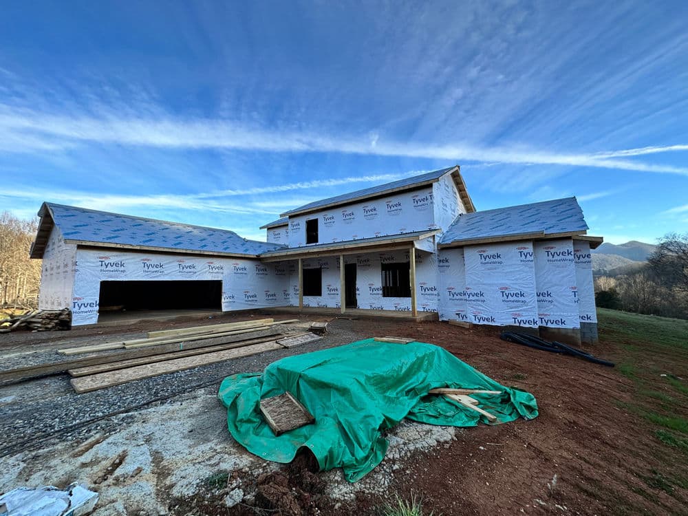 New house construction with Tyvek wrapping, unfinished exterior, and mountain backdrop.