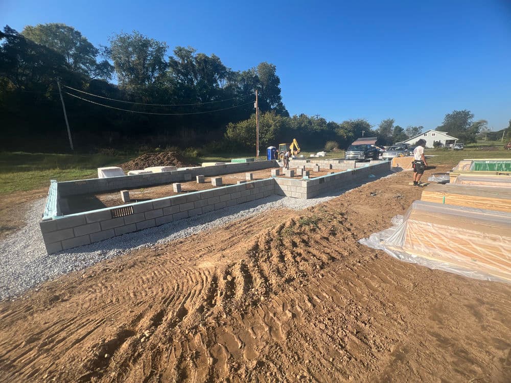 Construction site with cinder block foundation and workers under clear blue sky.