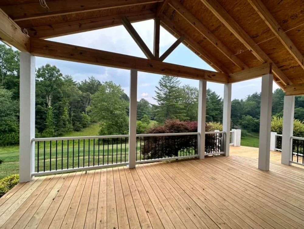 Spacious wooden porch with a scenic view of green trees and open fields.