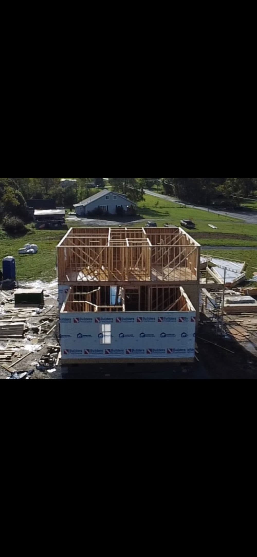 House under construction with wooden framing and surrounding building materials.
