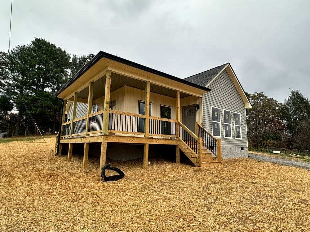 Newly built house with a front porch and wooden steps, surrounded by straw-covered ground.