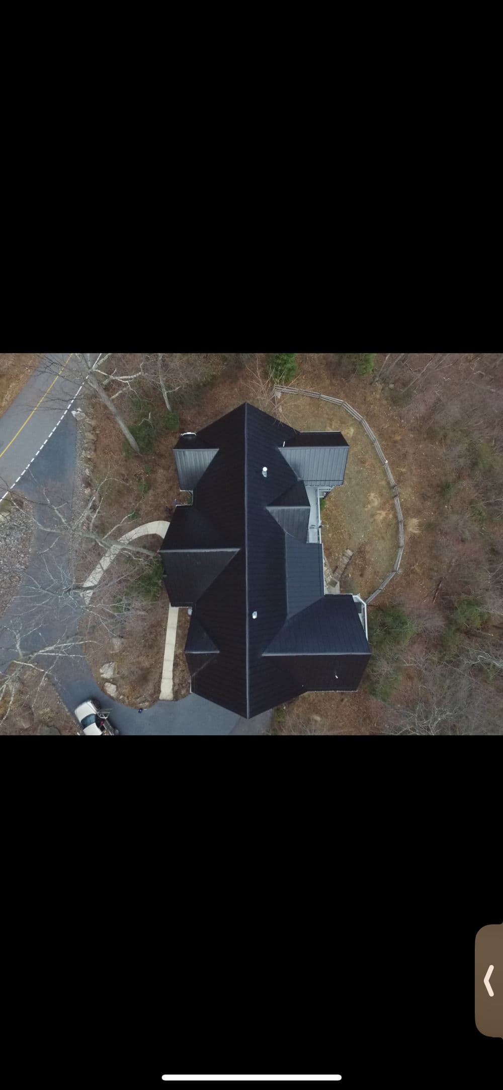 Aerial view of a large house with a black roof surrounded by trees and a winding driveway.